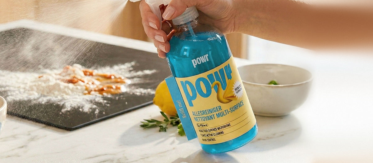 Hand spuit de POWR Allesreiniger op een aanrecht met bloem en saus, naast een citroen en een kommetje